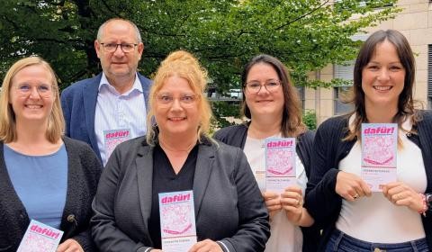 Vier Damen und ein Herr nebeneinander. Sie halten lächelnd ein Flugblatt in den Händen.