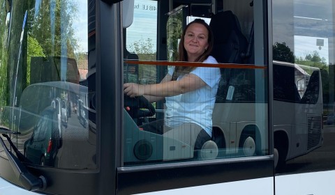 Eine Frau sitzt am Steuer eines Omnibusses. Der Omnibus ist unterhalb der Fahrerfensterscheibe mit dem Logo des Landkreises Ravensburg bedruckt.