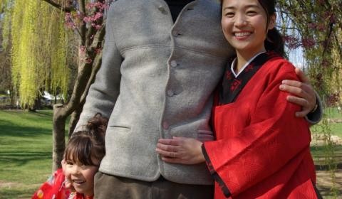 Ein Mann steht mit seiner Frau und der kleinen Tochter vor einem blühenden Kirschbaum.