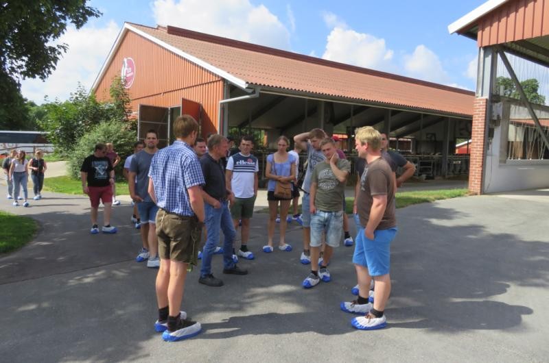 Milchviehbetrieb Derboven eine Gruppe junger Erwachsener steht auf dem Hofgelände eines Milchviehbetriebes, also vor einem Stallgebäude. Es herrscht sonniges Wetter.