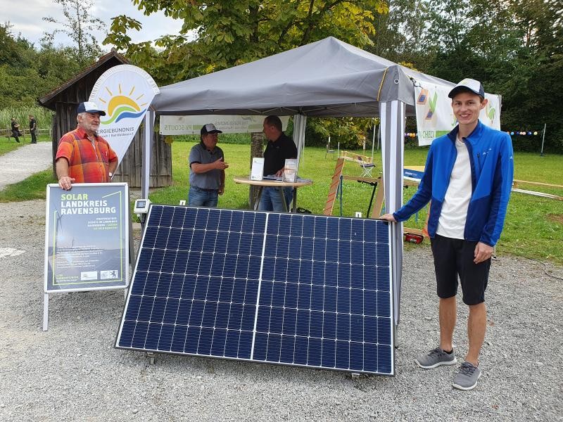 Vier beratende PV-Scouts an einem Informationsstand mit Solarmodul im Vordergrund