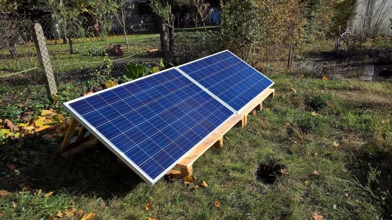 in einem Garten zwei Solarmodule - blaue Paneele - auf einem Holzpodest.