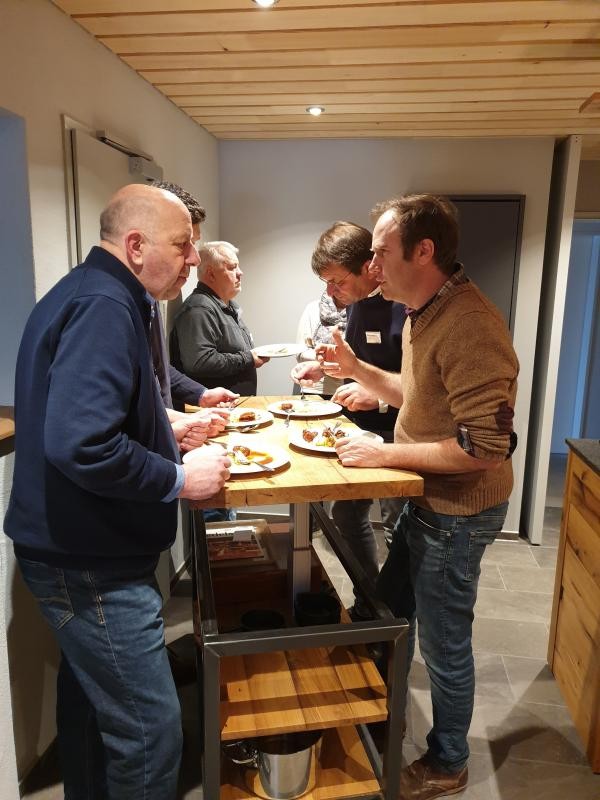 Männer stehen an einem Tisch und essen. Dabei sprechen sie miteinander.