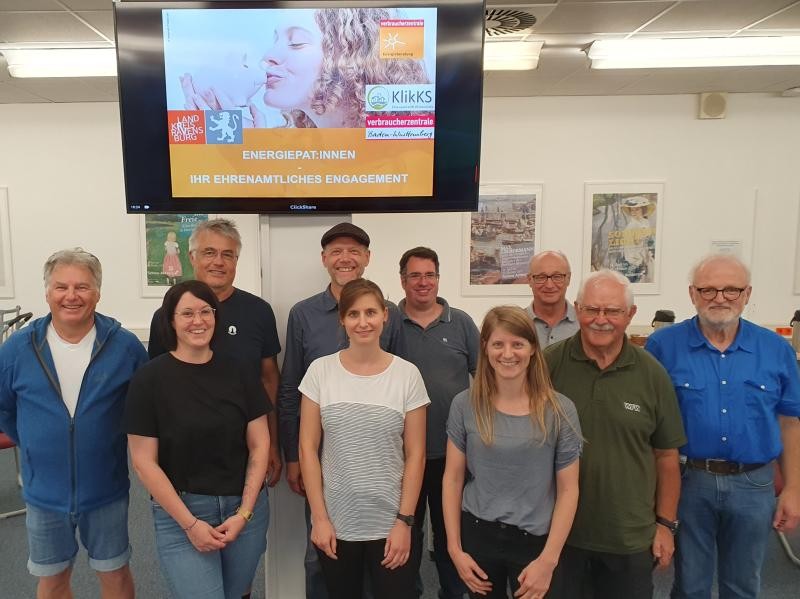 Energiepaten des Landkreises Ravensburg Zehn weibliche und männliche Personen stehen nebeneinander und blicken in die Kamera. Im Hintergrund ist ein Bildschirm zu sehen, auf dem mit dem Logo des Landkreises Ravensburg für den neuen Service geworben wird.