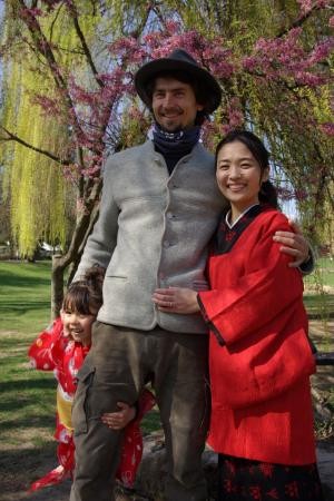 Ein Mann steht mit seiner Frau und der kleinen Tochter vor einem blühenden Kirschbaum.