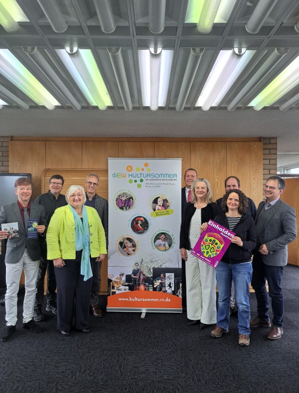 8. OEW-Kultursommer Menschen stehen neben einem Roll-Up-Werbeaufsteller und lächeln