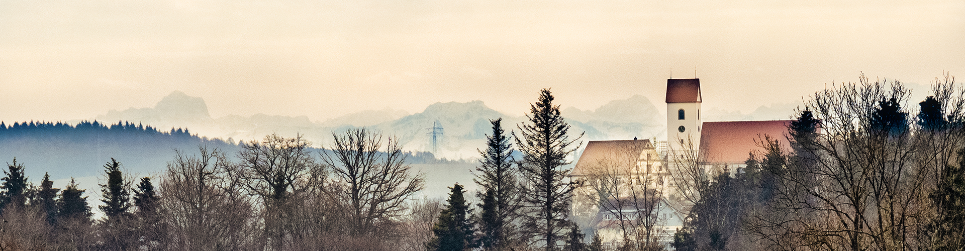 Panoramablick auf die Ortssilhouette der Gemeinde Berg. Im Hintergrund die Alpen. Es herrscht nebliges Wetter