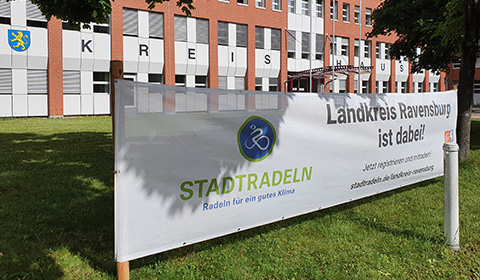 Vor einem Backsteinverwaltungsgebäude steht auf der Wiese davor ein Banner mit der Aufschrift Stadtradeln und Landkreis Ravensburg ist dabei.