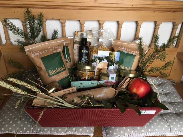 Beispiel eines Bio-Gschenkles Eine weihnachtlich mit Nadelbaumreisig dekorierte rechteckige Geschenkschale voller verschiedener Lebensmittel wie zum Beispiel Spätzle- und Dinkelmehl , Honig, Öl und Nudeln