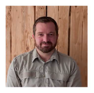 Porträtbild eines bärtigen hellbraunhaarigen hellhäutigen jungen Mannes in einem beigen Hemd